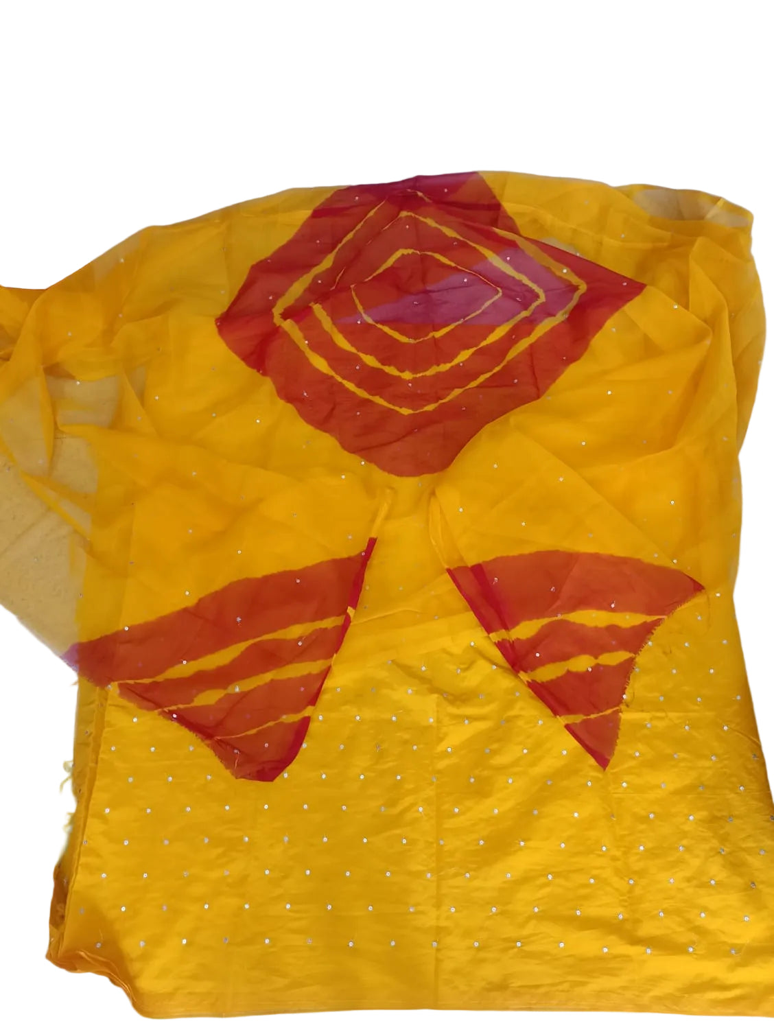 A yellow and red tie-dye fabric garment laid flat on a light-colored floor, featuring red geometric patterns and small silver embellishments.